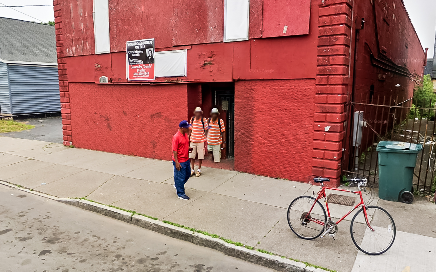 Deux homme avec un haut rouge devant un batiment de la même couleur. L'un d'eux, suite à un beugue, est dédoublé